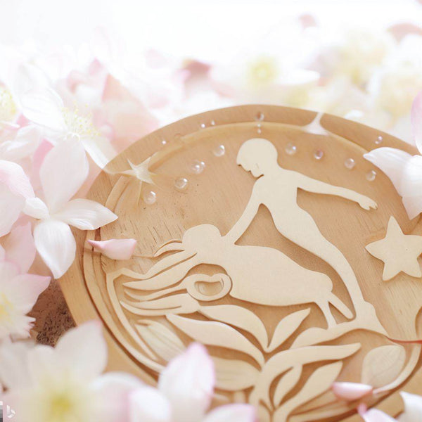Wooden artwork depicting two figures surrounded by soft flowers representing spiritual rebirthing therapy