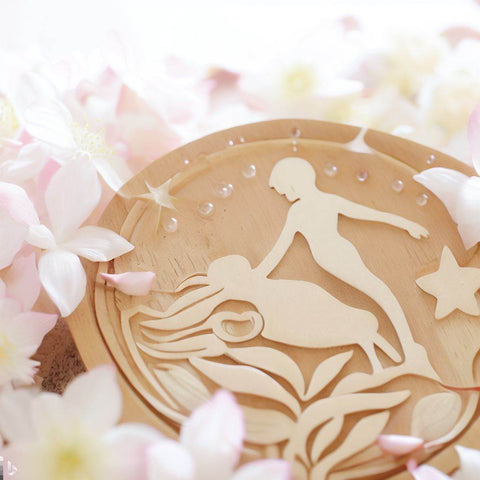 Wooden artwork depicting two figures surrounded by soft flowers representing spiritual rebirthing therapy